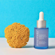 Rena Roots Albanian Immortelle Serum  bottle with dropper next to a yellow Immortelle Flower on a blue background