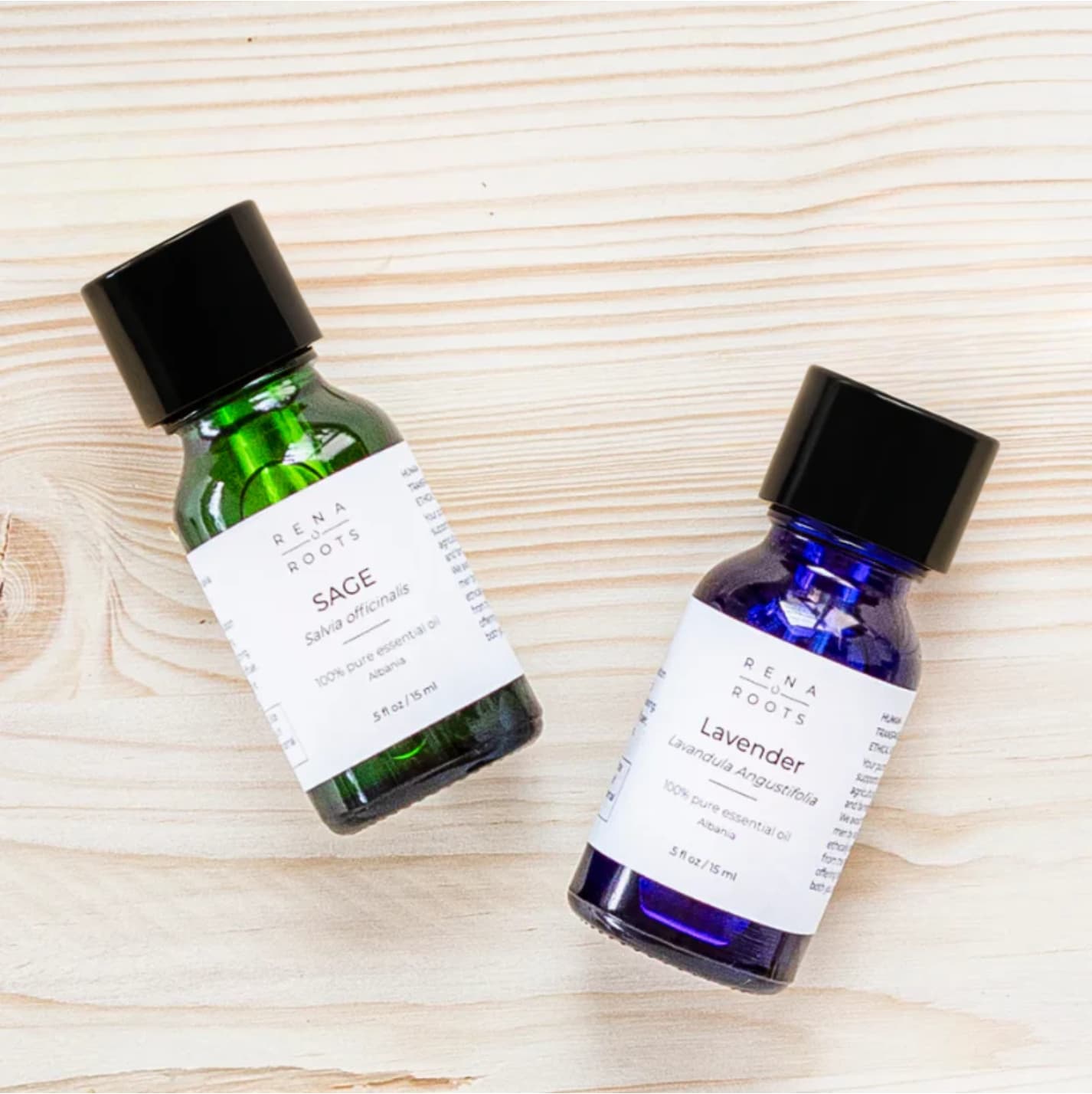 Two Rena Roots essential oil bottles, one green and one blue, labeled Sage and Lavender on a wooden surface.