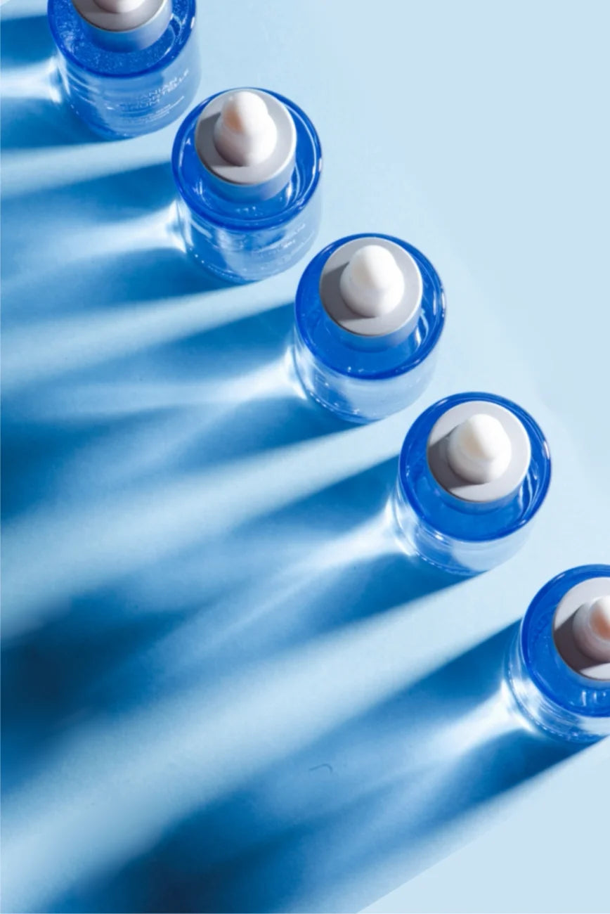 Five baby bottles with blue lids arranged on a light blue surface with shadows.