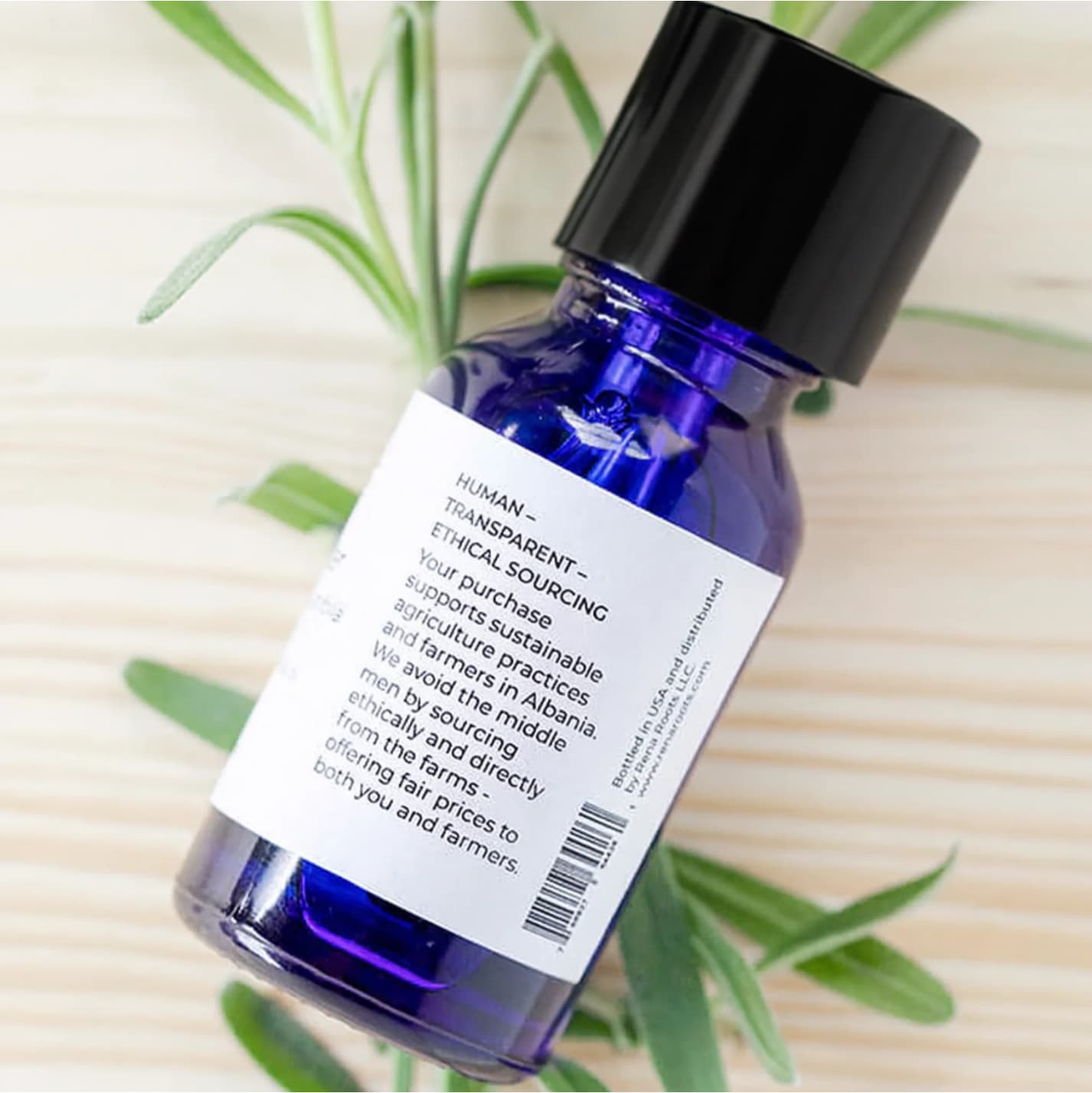 Blue Rena Roots Lavender Essential Oil bottle with a black cap on a light wooden surface with green leaves