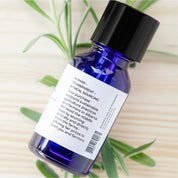 Blue Rena Roots Lavender Essential Oil bottle with a black cap on a light wooden surface with green leaves