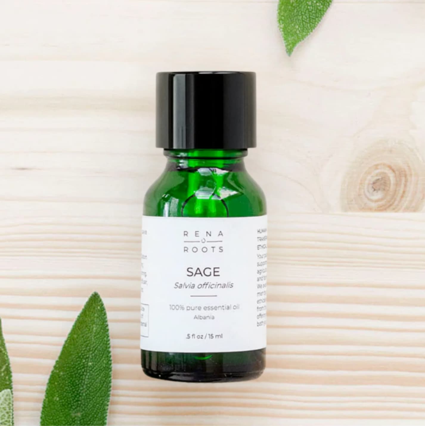 Bottle of Sage essential oil by Rena Roots on a wooden background with sage leaves.