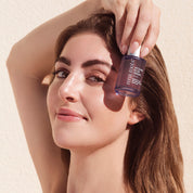 Woman holding a bottle of Rena Roots Afghan Rose Serum with a beige background