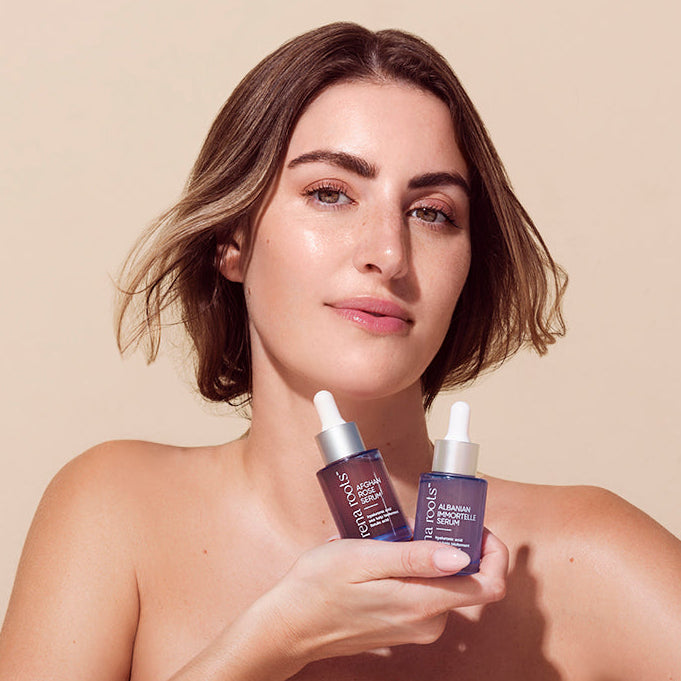 Woman holding two Rena Roots Serums against a beige background