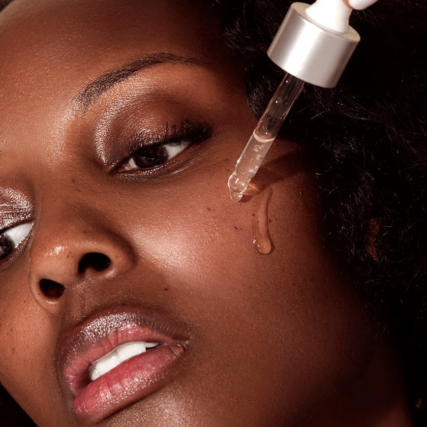 Close-up of a woman applying Rena Roots Serum to her face with a dropper.
