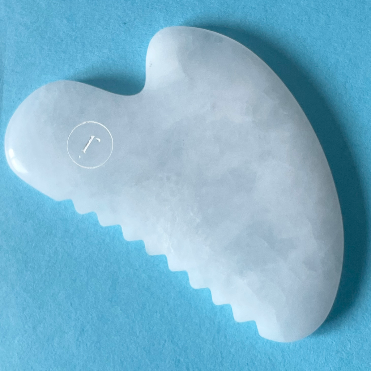 White Gua Sha tool with a brand logo on a blue background